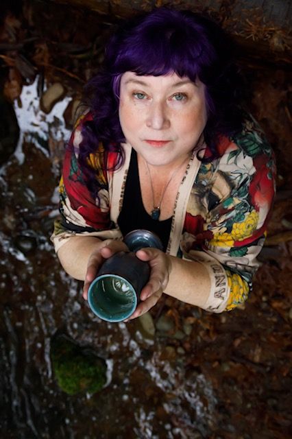 Paula holding a cup looking upwards.